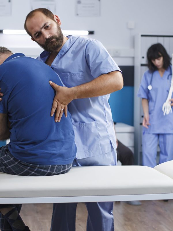 Osteopathic nurse gently extends spine of elderly patient with injury as part of physiotherapy. Chiropractor provides aid to gentleman experiencing back pains, aiding in physical recovery.